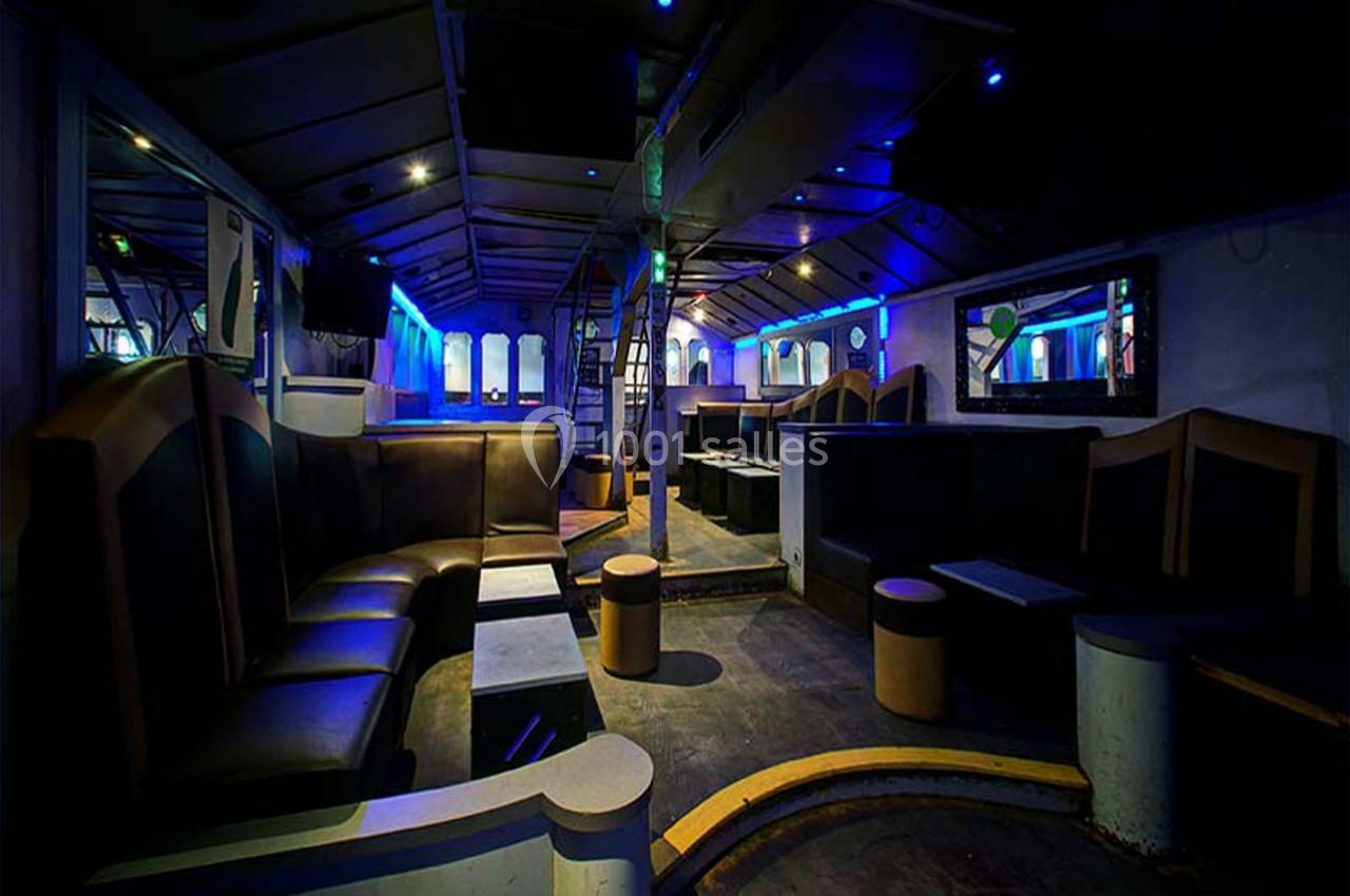 Intérieur d'une salle de réception moderne avec banquettes, tables basses et éclairage tamisé bleu.