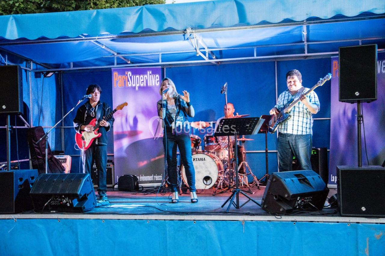 Groupe de musiciens jouant sur une scène extérieure, avec une chanteuse au centre et des instruments visibles.