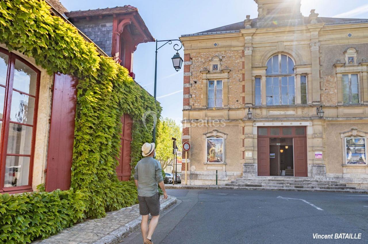 Un homme marche près d'un bâtiment historique en pierre et d'une maison couverte de lierre, sous un ciel ensoleillé.