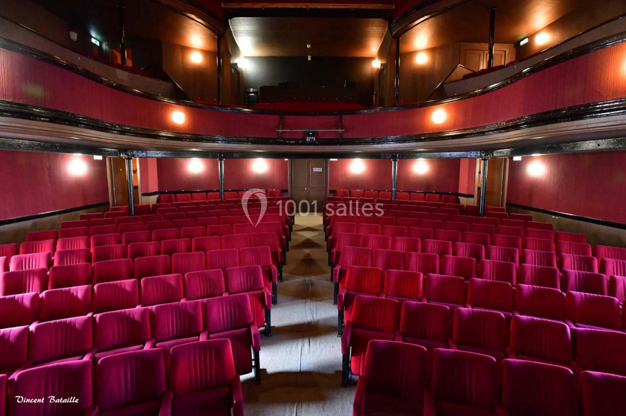 Salle de théâtre vide avec des rangées de fauteuils rouges et une scène en arrière-plan.
