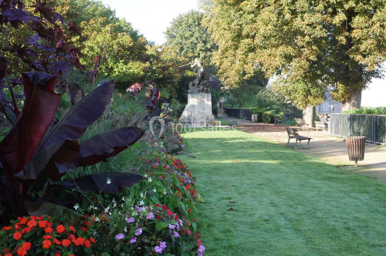 Allée bordée de fleurs colorées et de grands arbres, avec une statue en arrière-plan dans un parc.