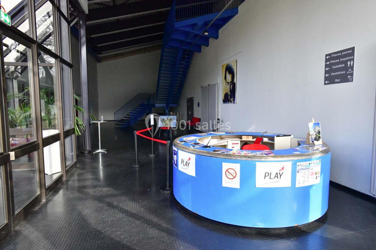 Accueil circulaire bleu dans un hall spacieux avec escalier métallique et panneaux d'information au mur.