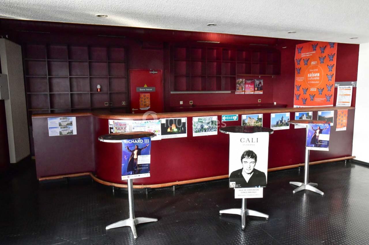 Un comptoir vide avec des affiches d'événements culturels et deux tables hautes dans un espace intérieur.