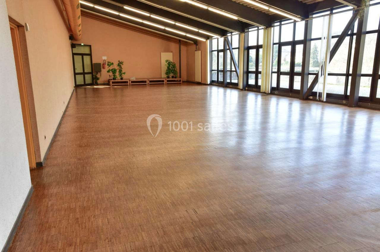 Salle spacieuse avec parquet en bois, grandes baies vitrées et quelques plantes en arrière-plan.