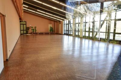 Salle spacieuse avec parquet en bois, grandes baies vitrées et quelques plantes en arrière-plan.