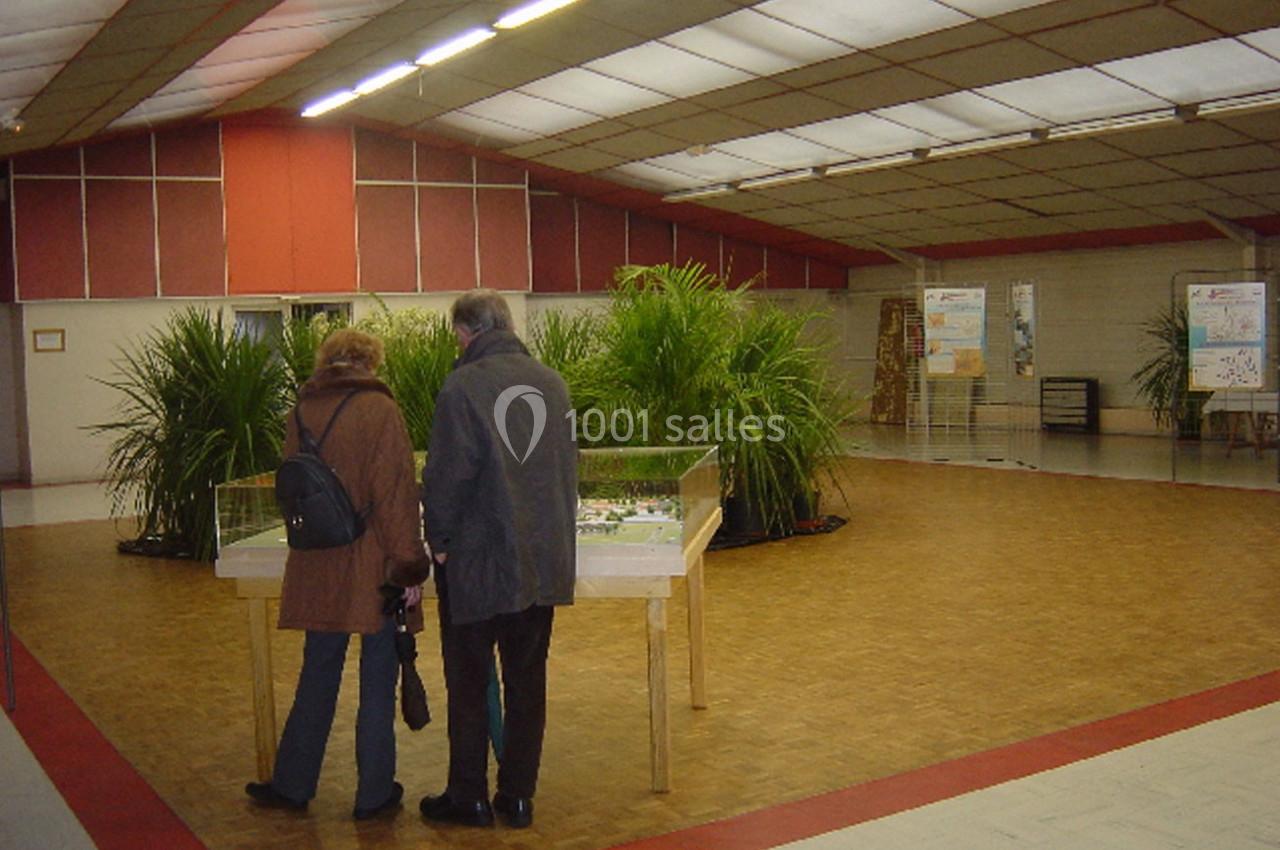 Deux personnes observent une maquette sous vitrine dans une salle avec des plantes et des panneaux d'exposition.