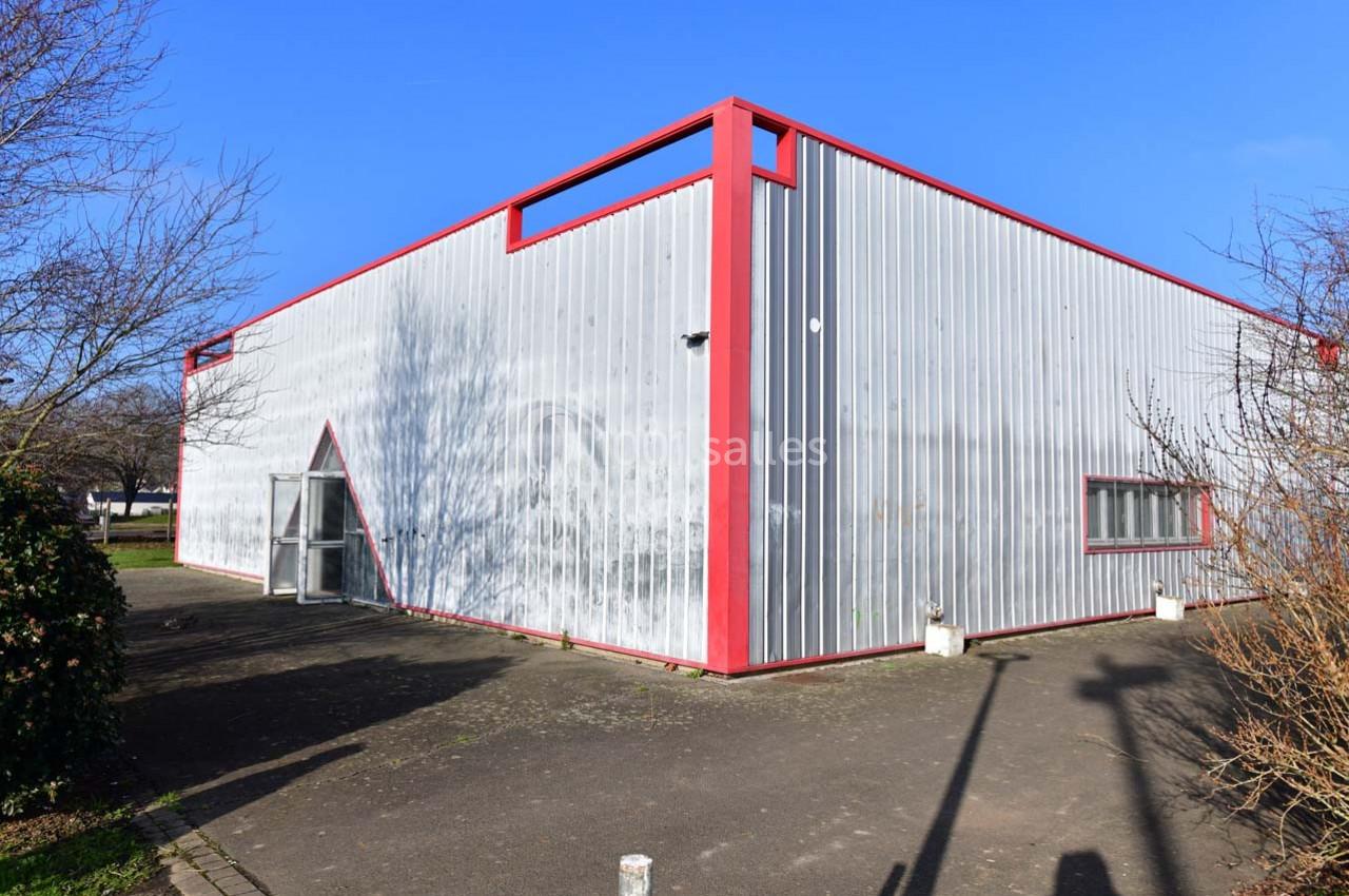 Bâtiment en métal gris avec des encadrements rouges, entouré d'arbres et d'une allée pavée sous un ciel bleu.
