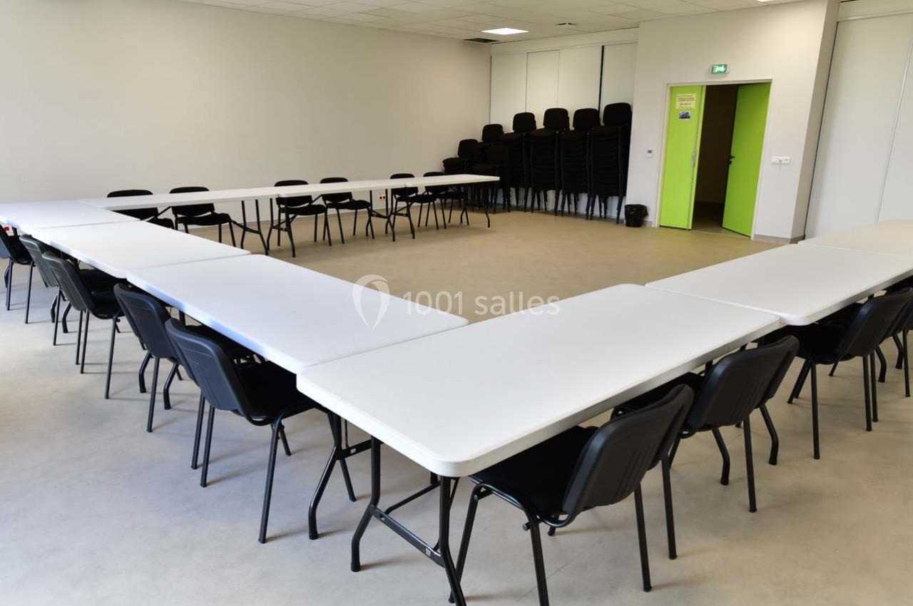 Salle de réunion avec des tables disposées en U, entourées de chaises noires empilées et alignées.
