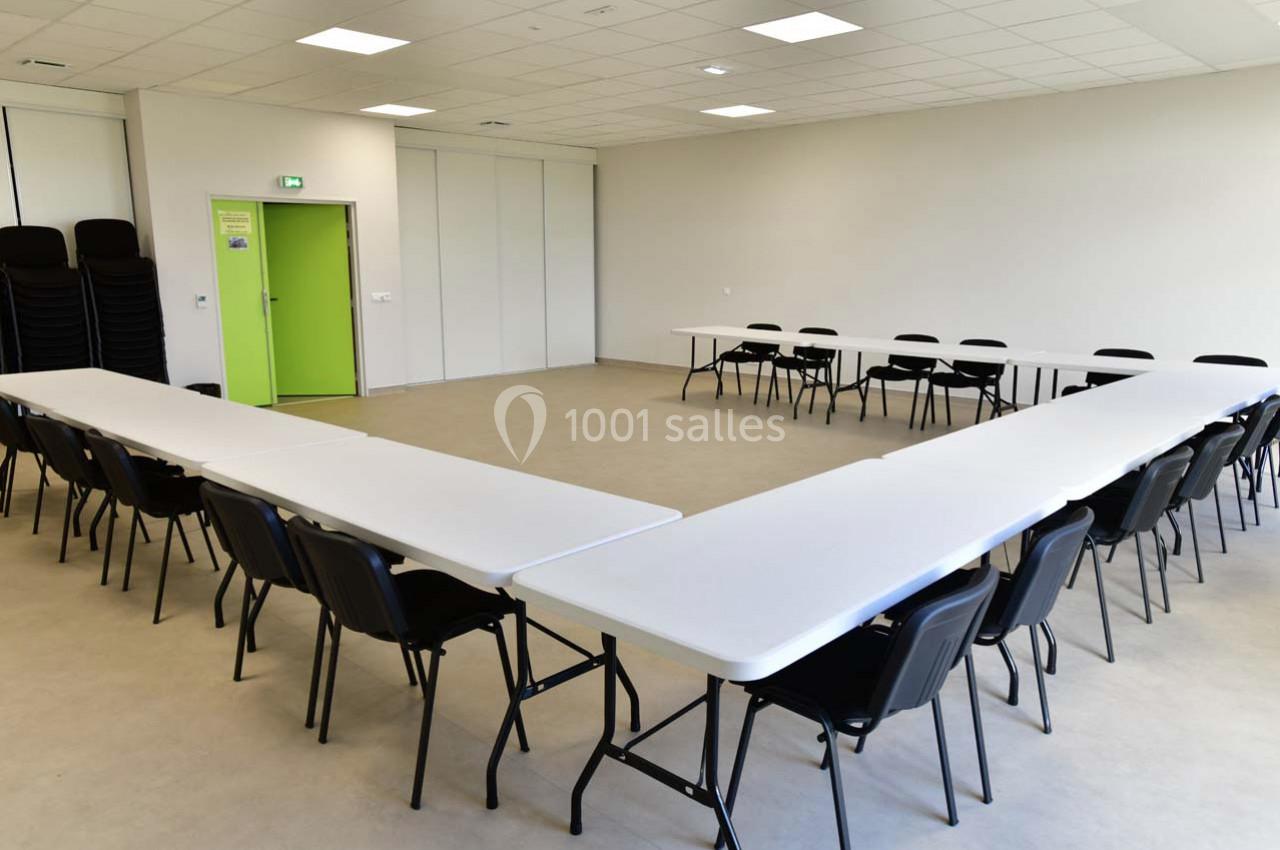Salle de réunion lumineuse avec des tables blanches disposées en U et des chaises noires.