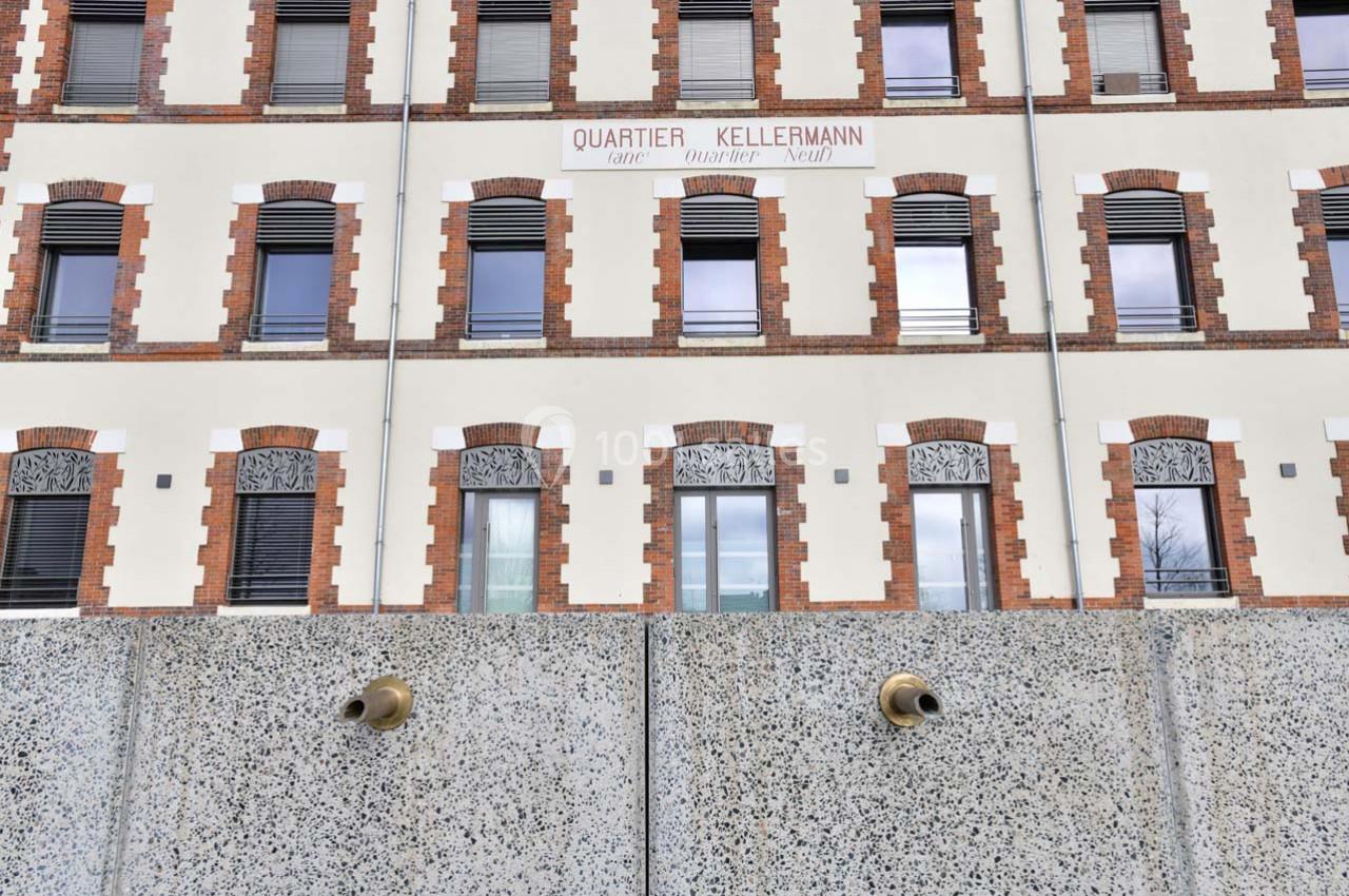 Façade d'un bâtiment en briques et crépi avec des fenêtres alignées, vue derrière un mur en béton.