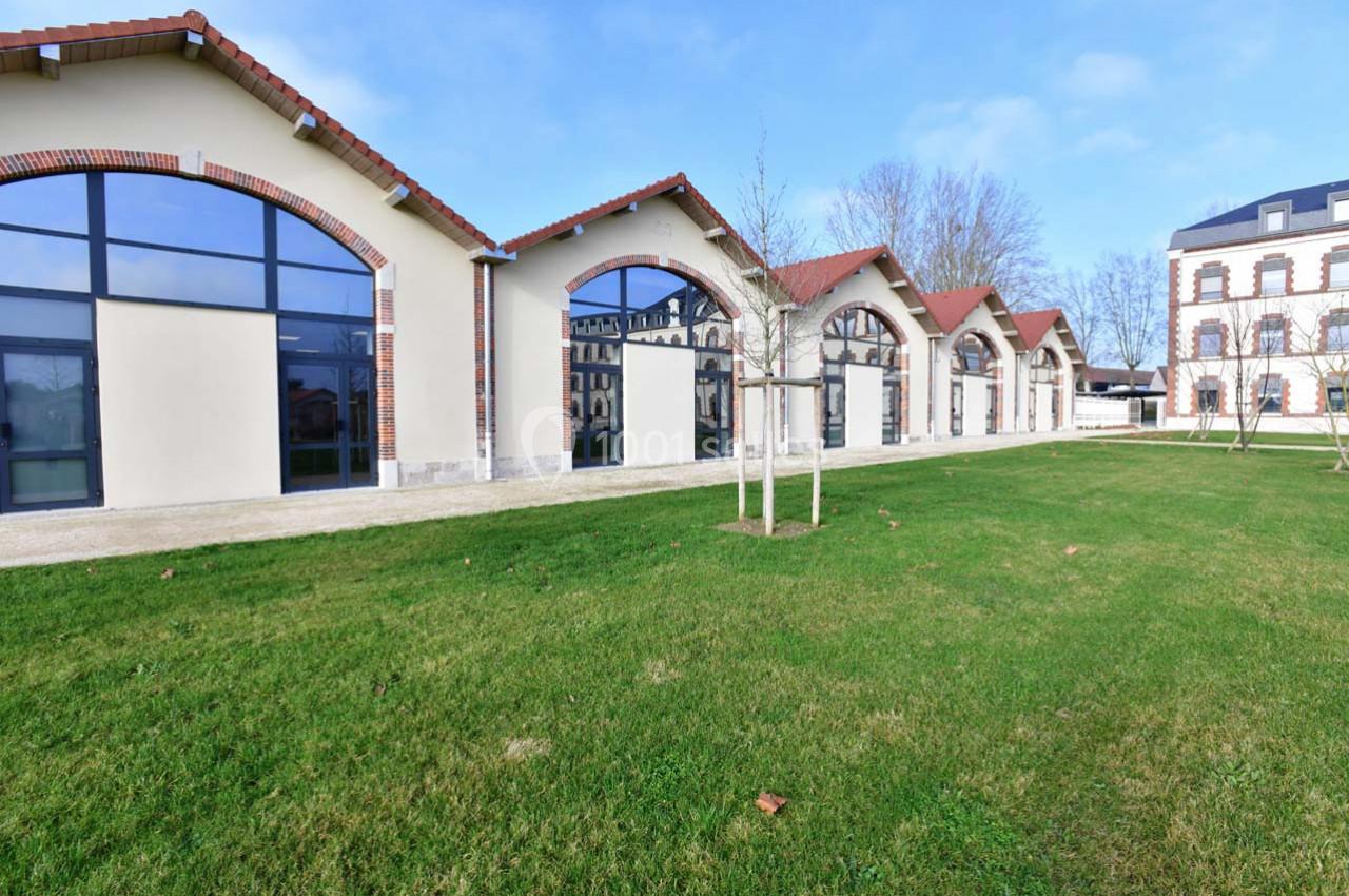 Bâtiments rénovés avec grandes baies vitrées en arc, bordés d'une pelouse et d'arbres, sous un ciel dégagé.
