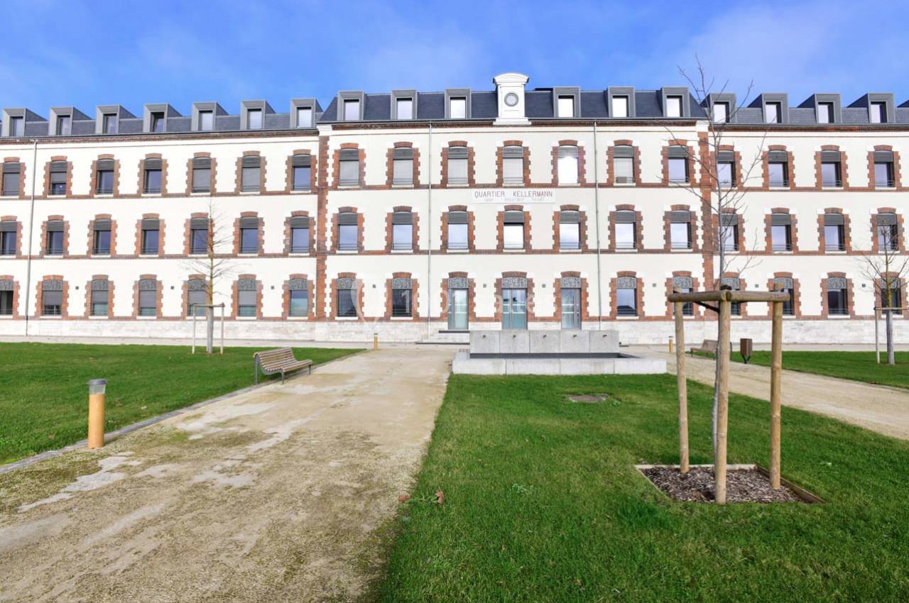 Façade d'un bâtiment rénové en briques blanches et rouges, entouré d'une pelouse et de chemins piétonniers.