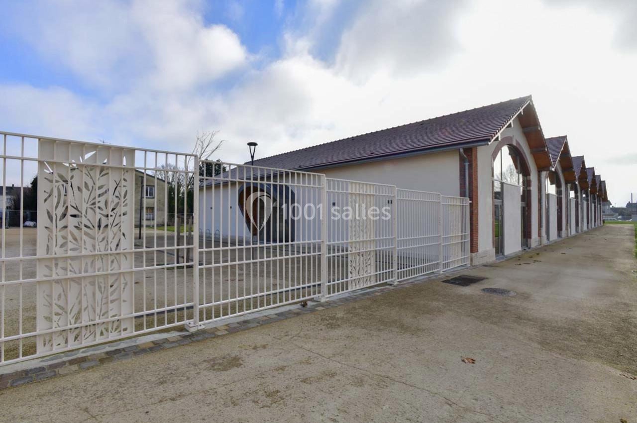 Clôture blanche en métal avec motifs végétaux devant un bâtiment à arcades et toit en tuiles sous un ciel partiellement…