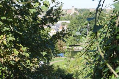 Façade d'un bâtiment historique en pierre blanche partiellement cachée par des arbres dans un jardin ensoleillé.