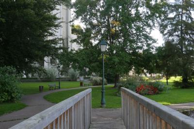 Façade d'un bâtiment historique en pierre blanche partiellement cachée par des arbres dans un jardin ensoleillé.