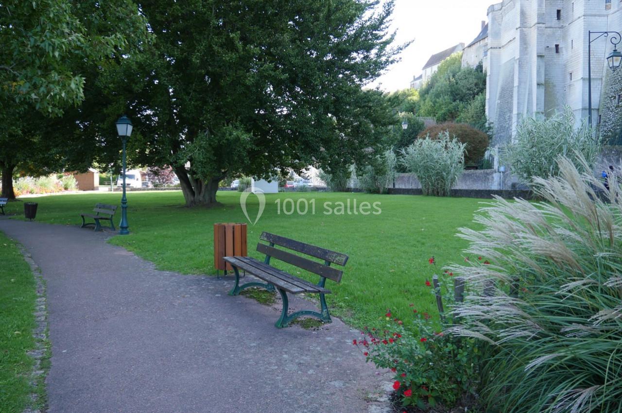 Allée bordée de bancs, arbres et pelouse, avec un bâtiment historique en arrière-plan.