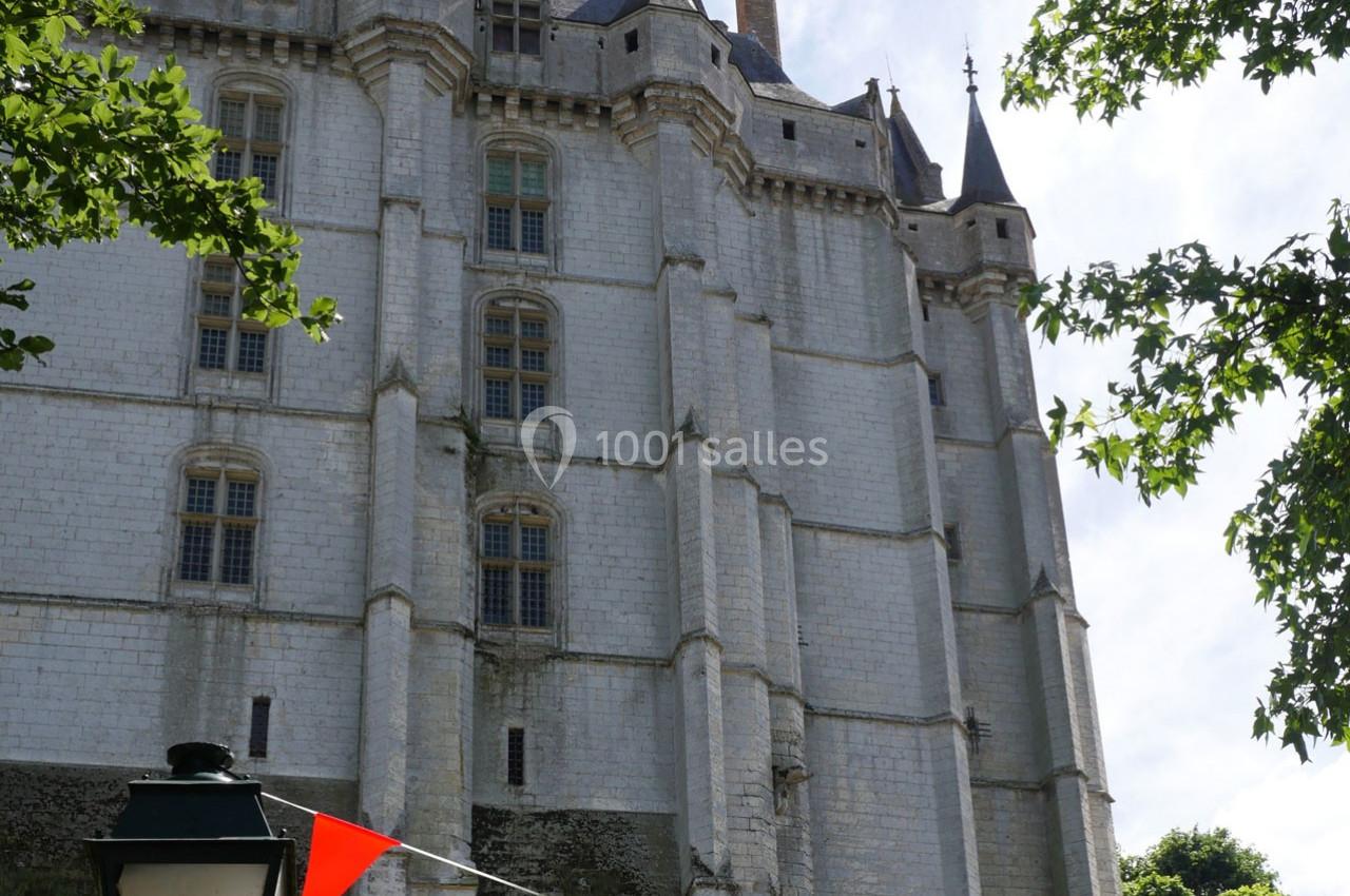 Façade d'un château en pierre blanche avec des tours et des fenêtres, entouré de verdure et de fanions colorés.