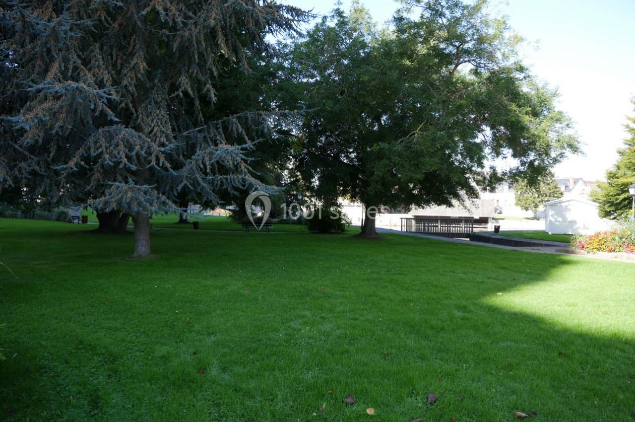 Pelouse verdoyante entourée d'arbres avec un chemin pavé et des bâtiments en arrière-plan.