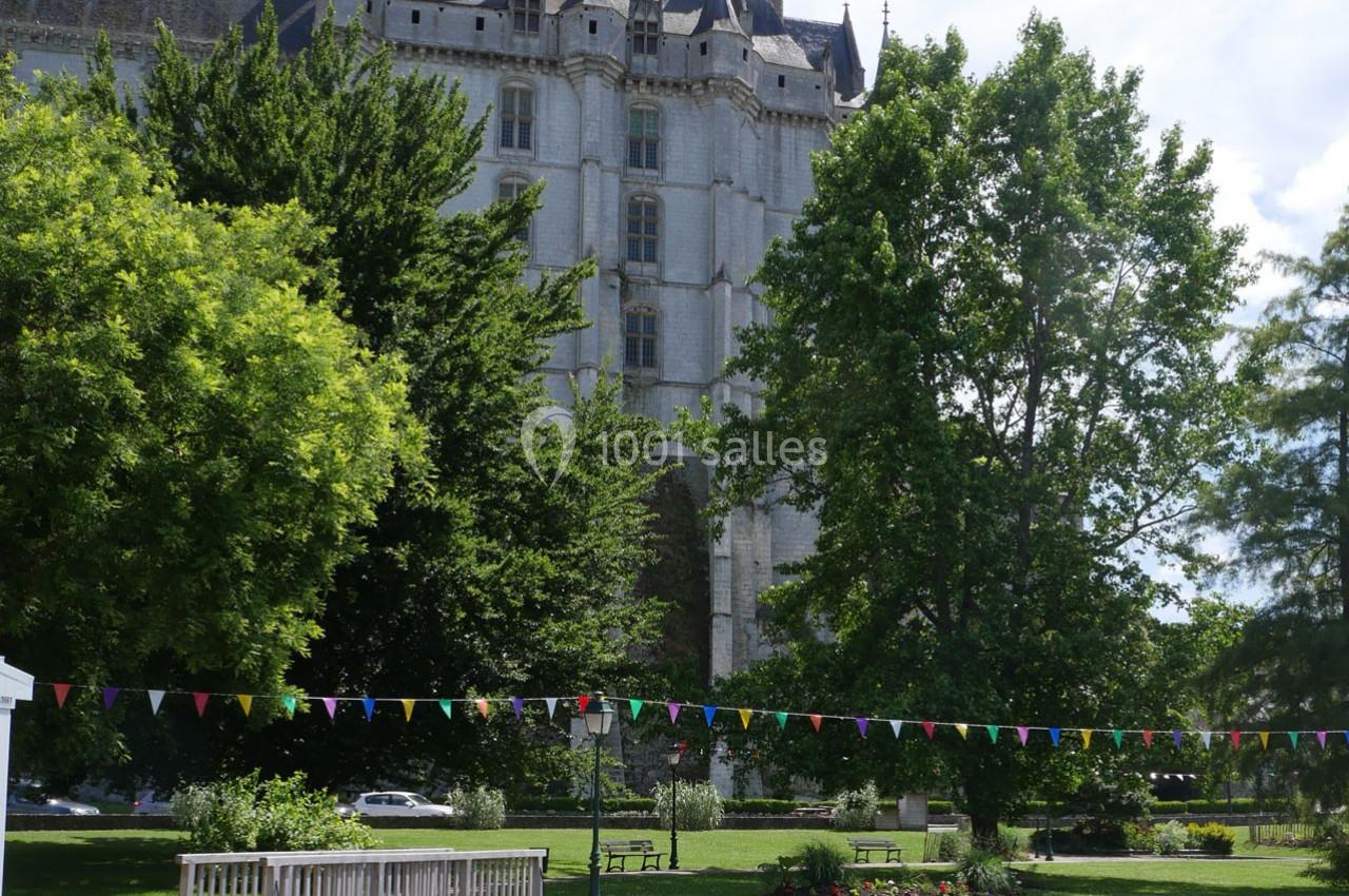 Façade d'un château en pierre entourée d'arbres, avec un parc aménagé et des guirlandes colorées au premier plan.