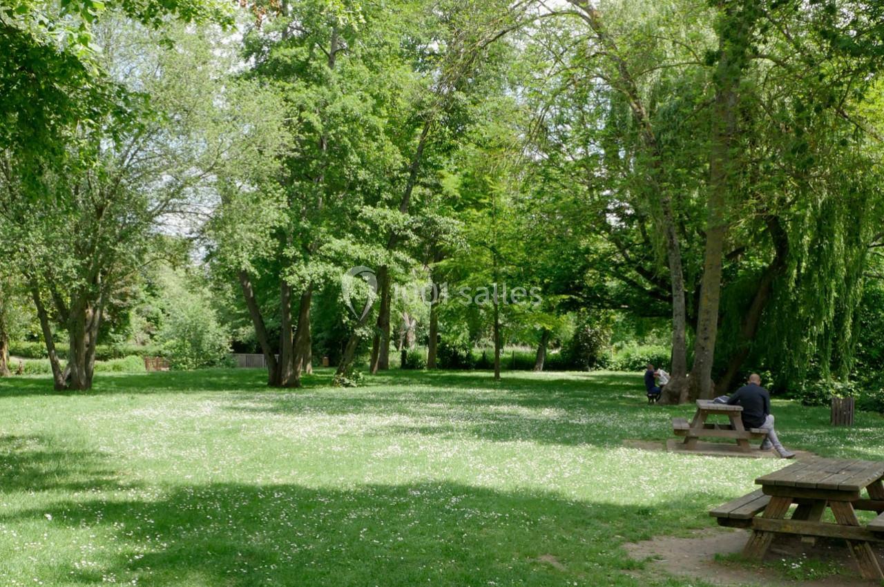 Espace vert avec pelouse, arbres et tables de pique-nique, deux personnes assises dans un cadre calme et ombragé.