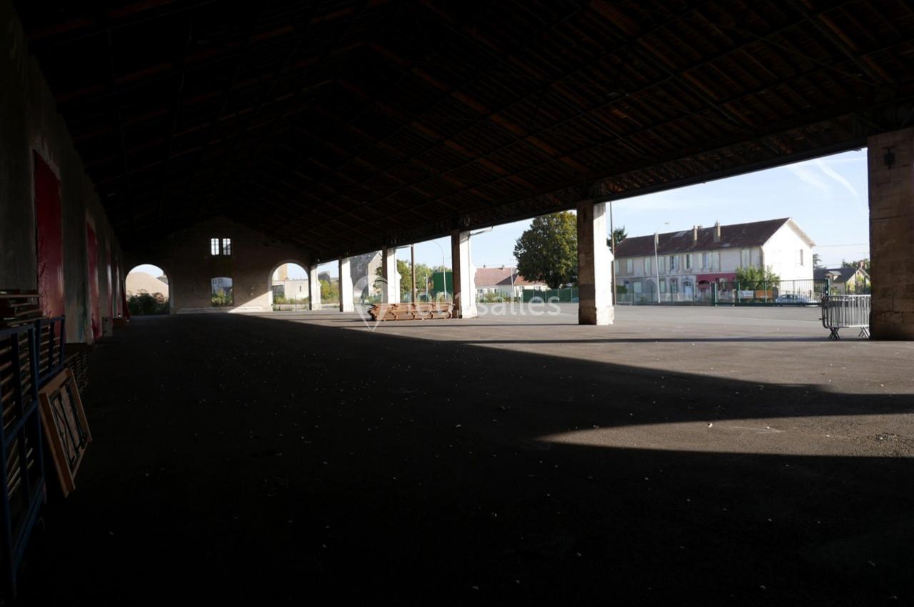 Vue d'un grand hangar ouvert avec une cour pavée et des bâtiments résidentiels en arrière-plan.