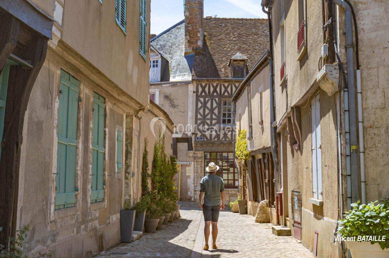 Un homme marche dans une ruelle pavée bordée de maisons anciennes à colombages et volets colorés.