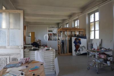 Atelier d'artiste lumineux avec tables de travail, matériel de peinture, étagères et une toile en cours.