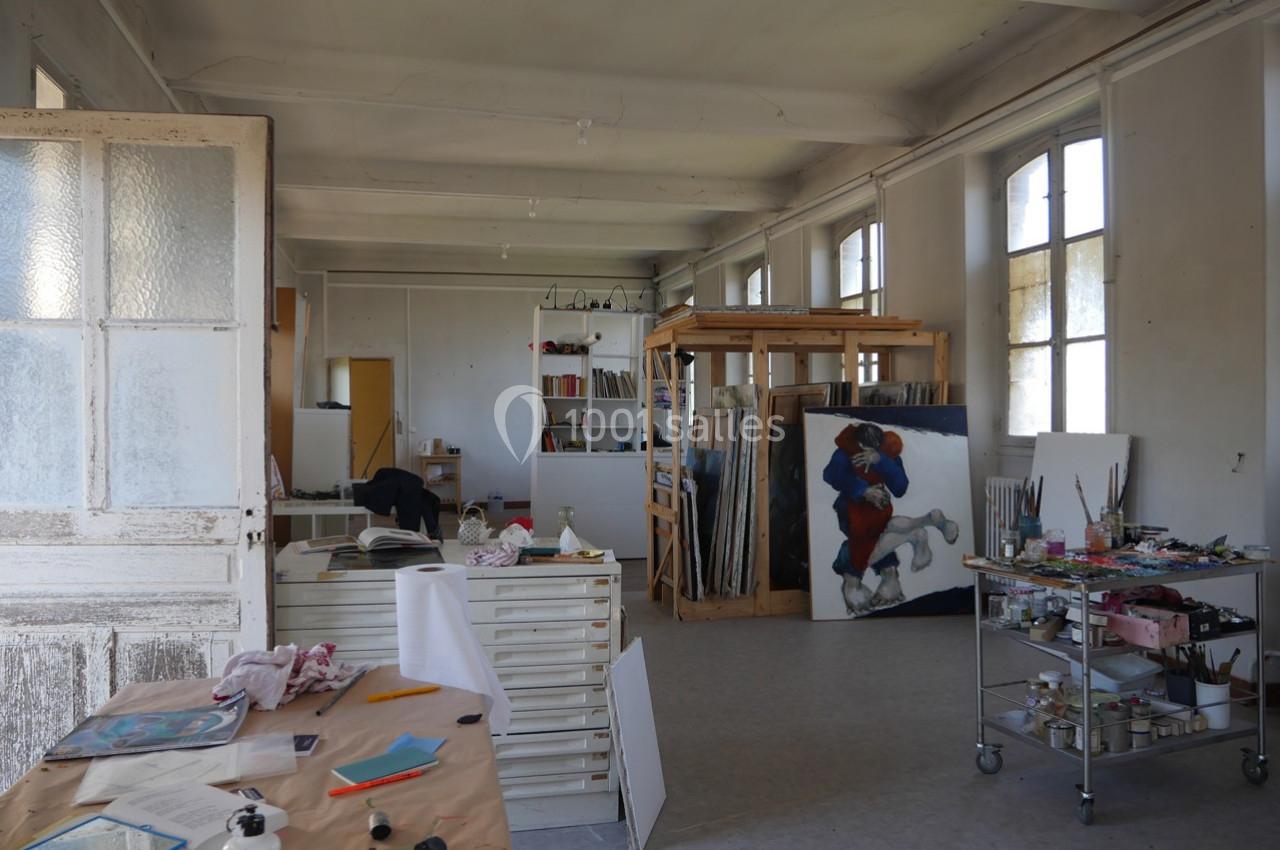 Atelier d'art lumineux avec des tables de travail, des étagères, des peintures et du matériel artistique.