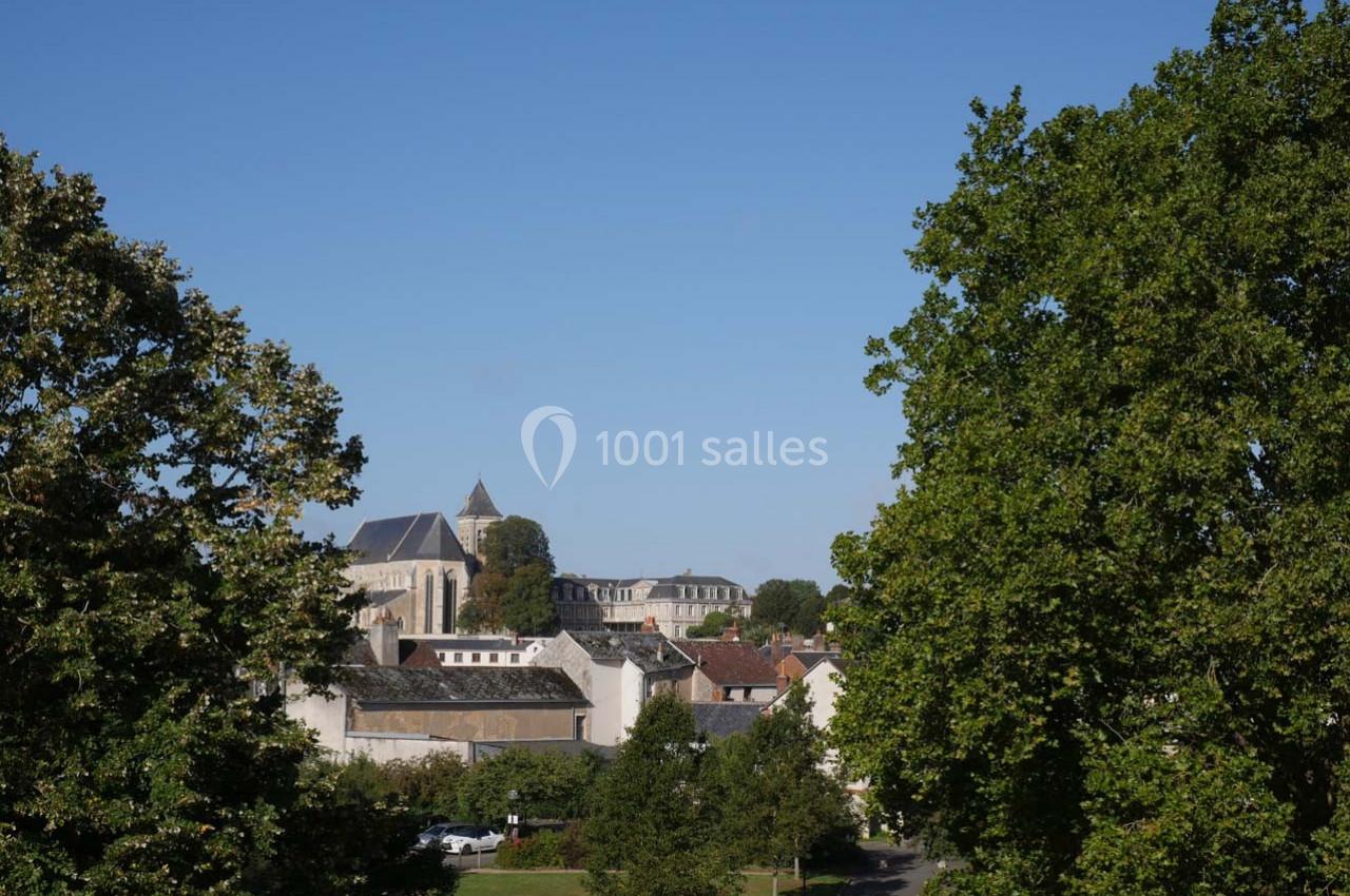 Vue d'un village avec des bâtiments anciens, une église et des arbres encadrant la scène sous un ciel bleu.