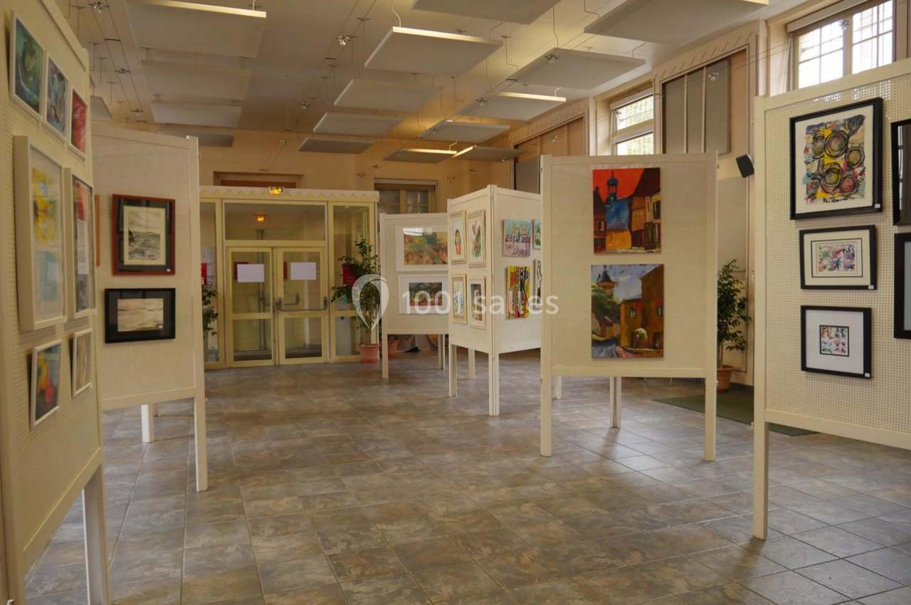 Salle d'exposition avec des peintures et dessins encadrés présentés sur des panneaux blancs.