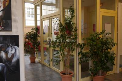 Entrée vitrée d'un bâtiment avec des plantes en pot et des peintures accrochées aux murs.