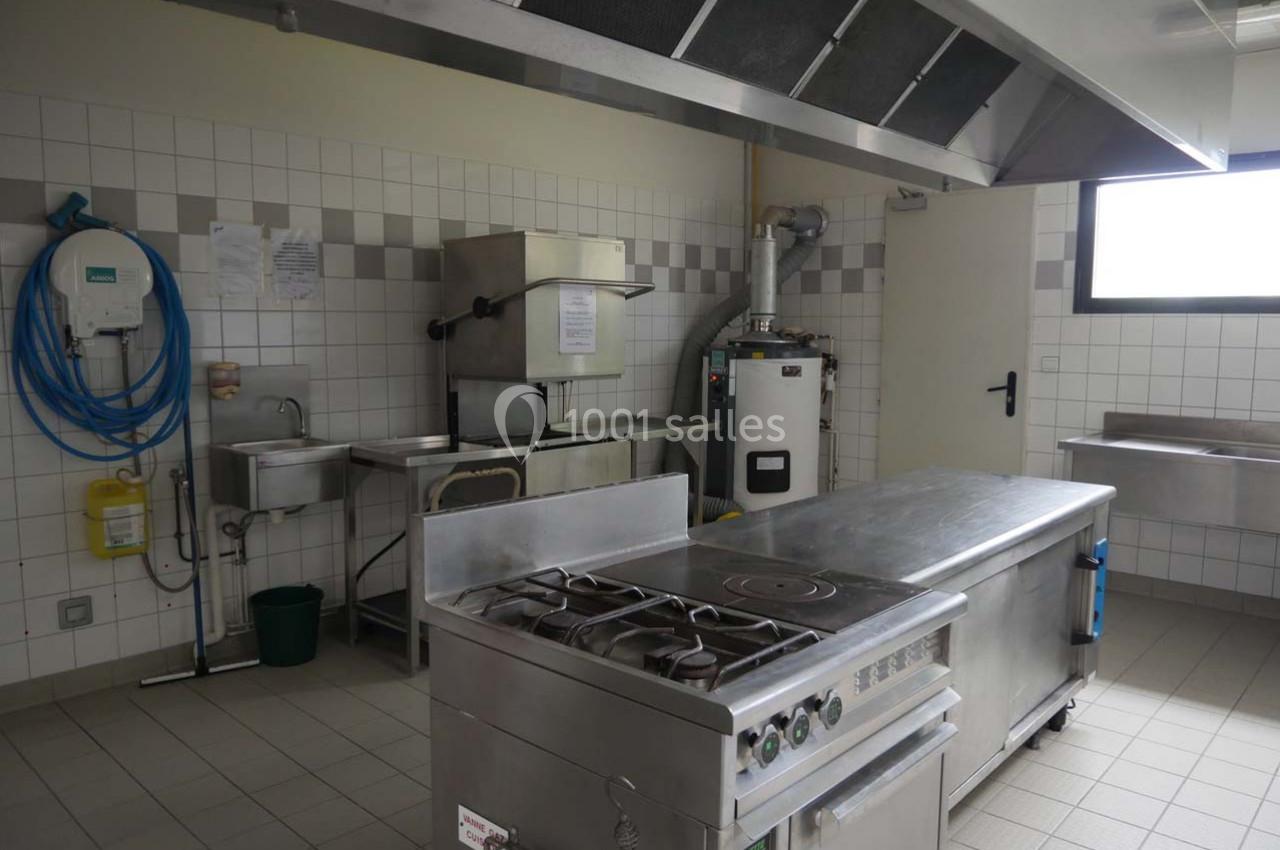 Cuisine professionnelle avec plan de travail en inox, cuisinière, évier, hotte et équipements muraux dans un espace carrelé.