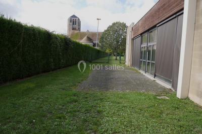 Salle vide avec parquet en bois, murs clairs, plafond avec poutres apparentes et grandes baies vitrées.