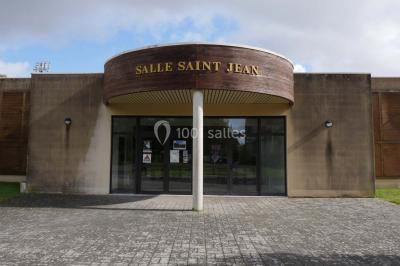 Salle vide avec parquet en bois, murs clairs, plafond avec poutres apparentes et grandes baies vitrées.