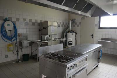 Salle vide avec parquet en bois, murs clairs, plafond avec poutres apparentes et grandes baies vitrées.