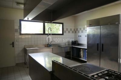 Salle vide avec parquet en bois, murs clairs, plafond avec poutres apparentes et grandes baies vitrées.