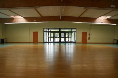 Salle vide avec parquet en bois, murs clairs, plafond avec poutres apparentes et grandes baies vitrées.