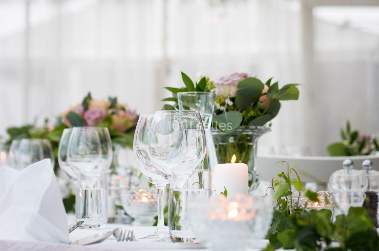 Table élégamment dressée avec verres, bougies allumées et compositions florales dans un cadre lumineux.