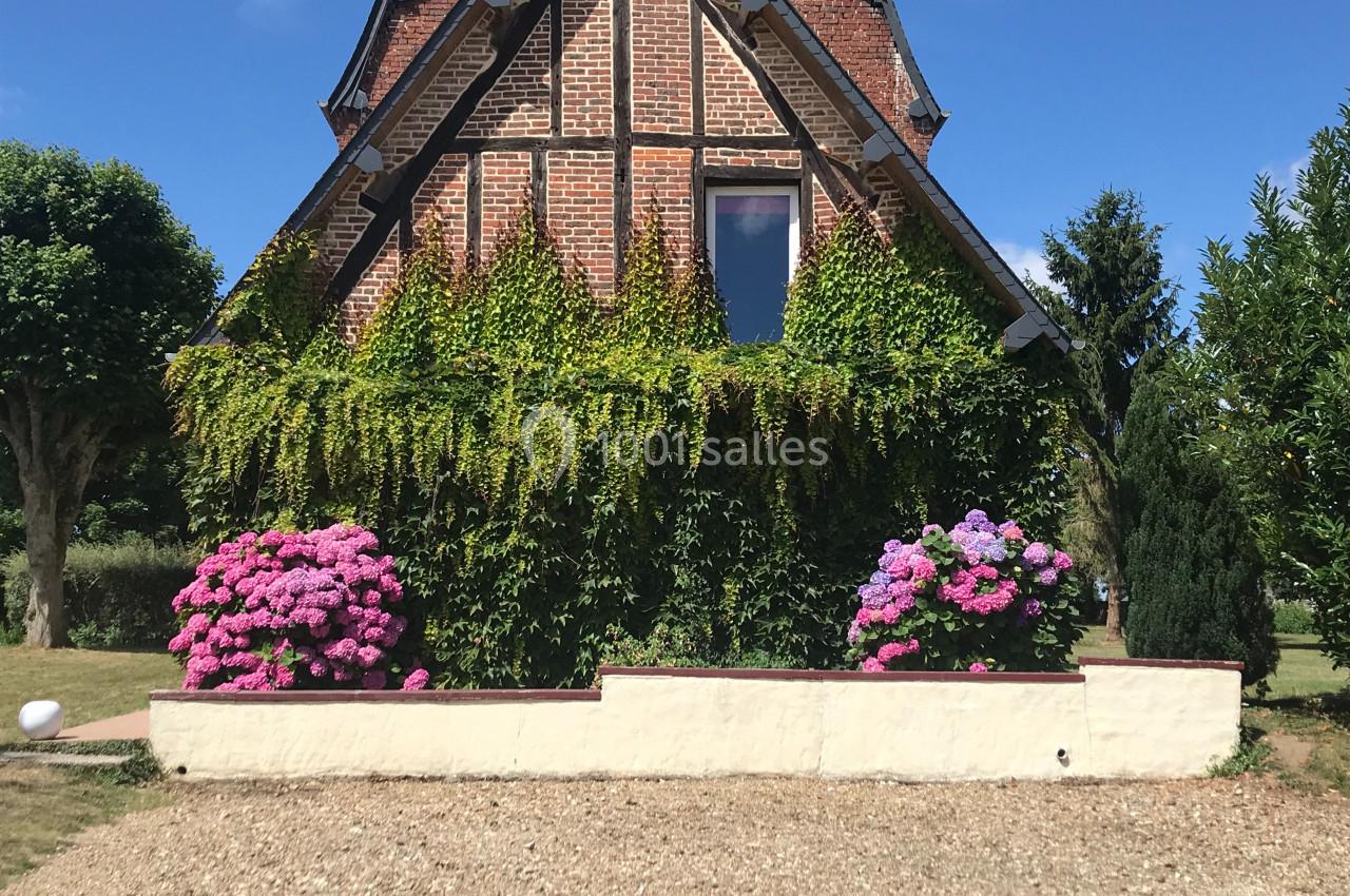 Façade en briques d'une maison à colombages, entourée de verdure et de massifs d'hortensias roses et violets.