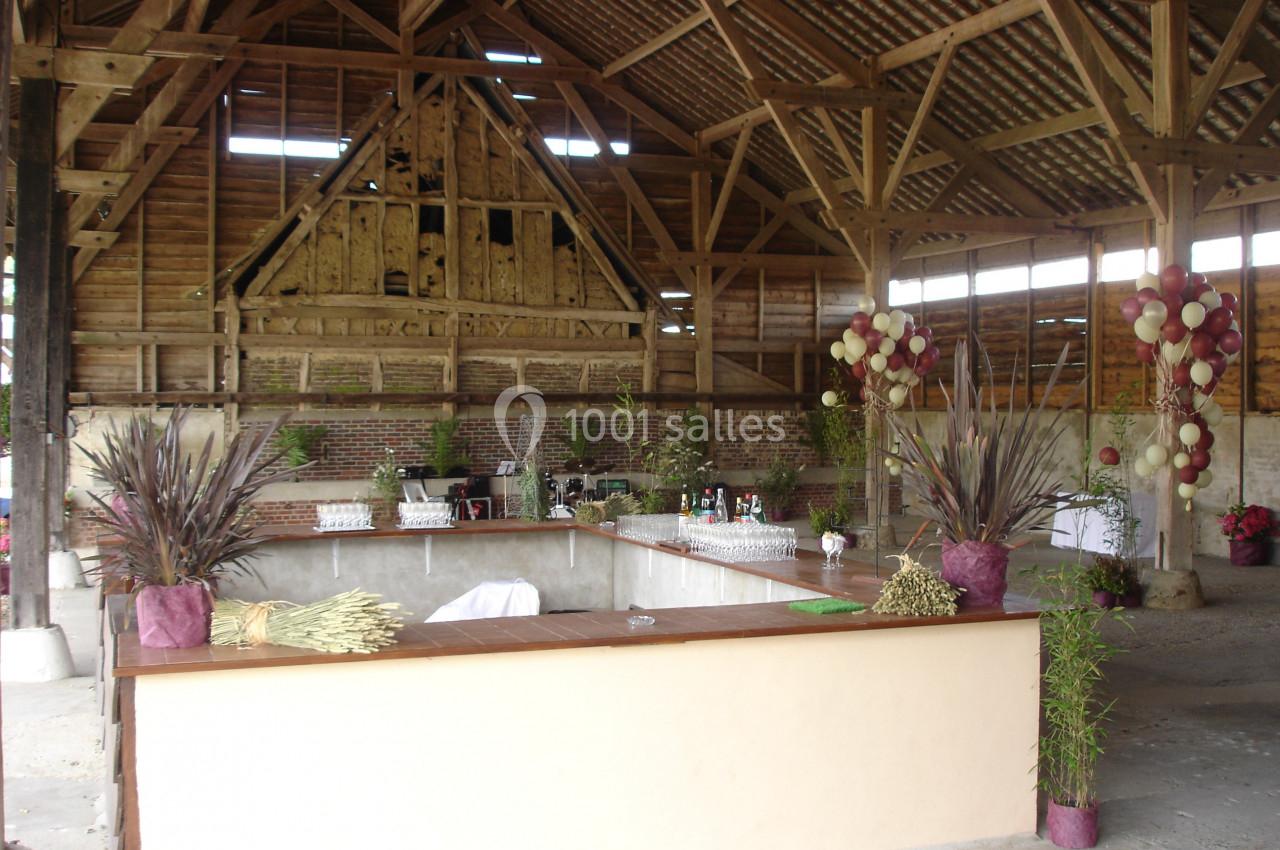 Intérieur d'une grange aménagée avec un bar en bois, des décorations végétales et des ballons colorés.