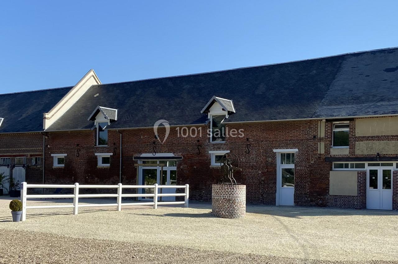 Bâtiment en briques rouges avec toit en ardoise, entouré d'une cour gravillonnée et de quelques plantes décoratives.
