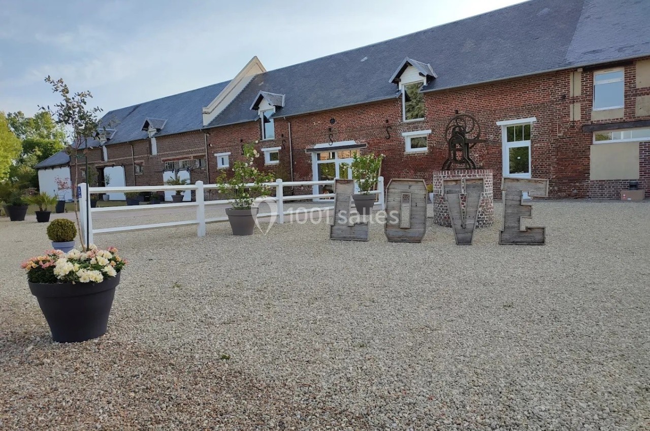 Cour d'une ferme rénovée avec façade en briques, décorée de grandes lettres formant ’LOVE’ et de pots de fleurs.