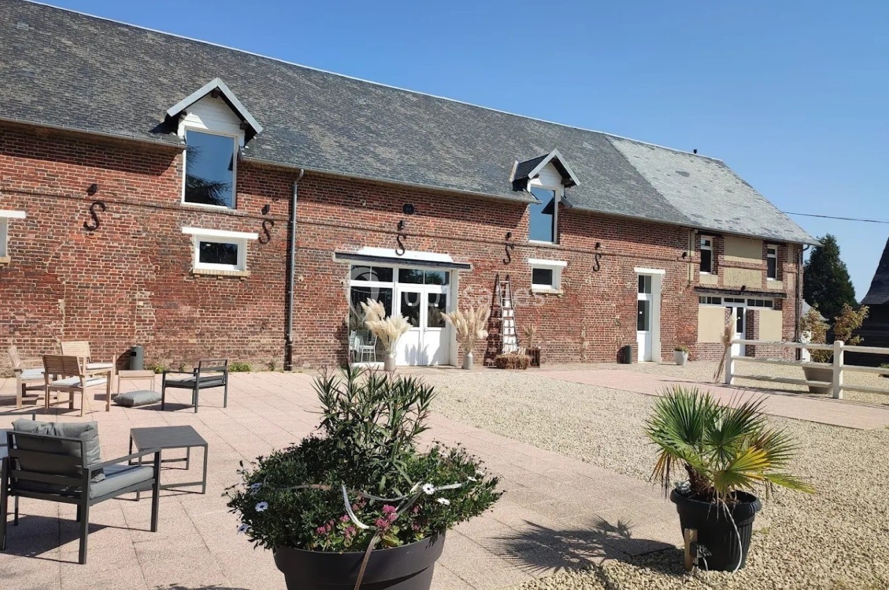 Cour pavée avec mobilier de jardin, plantes en pot et façade en briques d'un bâtiment à toit en ardoise.