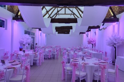 Allée en gravier bordée d'un bâtiment en bois et briques, décorée de fleurs et de voilages blancs.