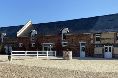 Allée en gravier bordée d'un bâtiment en bois et briques, décorée de fleurs et de voilages blancs.