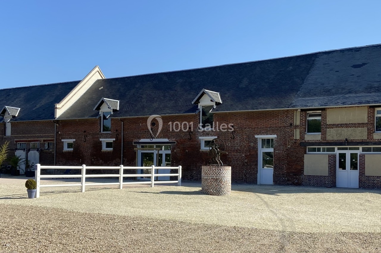 Bâtiment en briques rouges avec toit en ardoise, entouré d'une cour gravillonnée et de quelques plantes en pots.