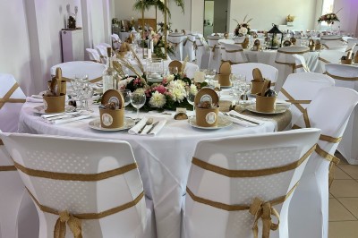 Allée en gravier bordée d'un bâtiment en bois et briques, décorée de fleurs et de voilages blancs.