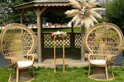 Allée en gravier bordée d'un bâtiment en bois et briques, décorée de fleurs et de voilages blancs.