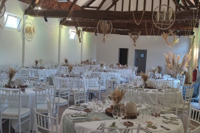Allée en gravier bordée d'un bâtiment en bois et briques, décorée de fleurs et de voilages blancs.