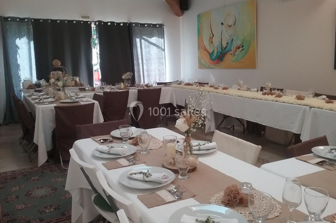 Salle décorée pour un repas festif avec tables dressées, nappes blanches, chemins de table en toile de jute et décorations…